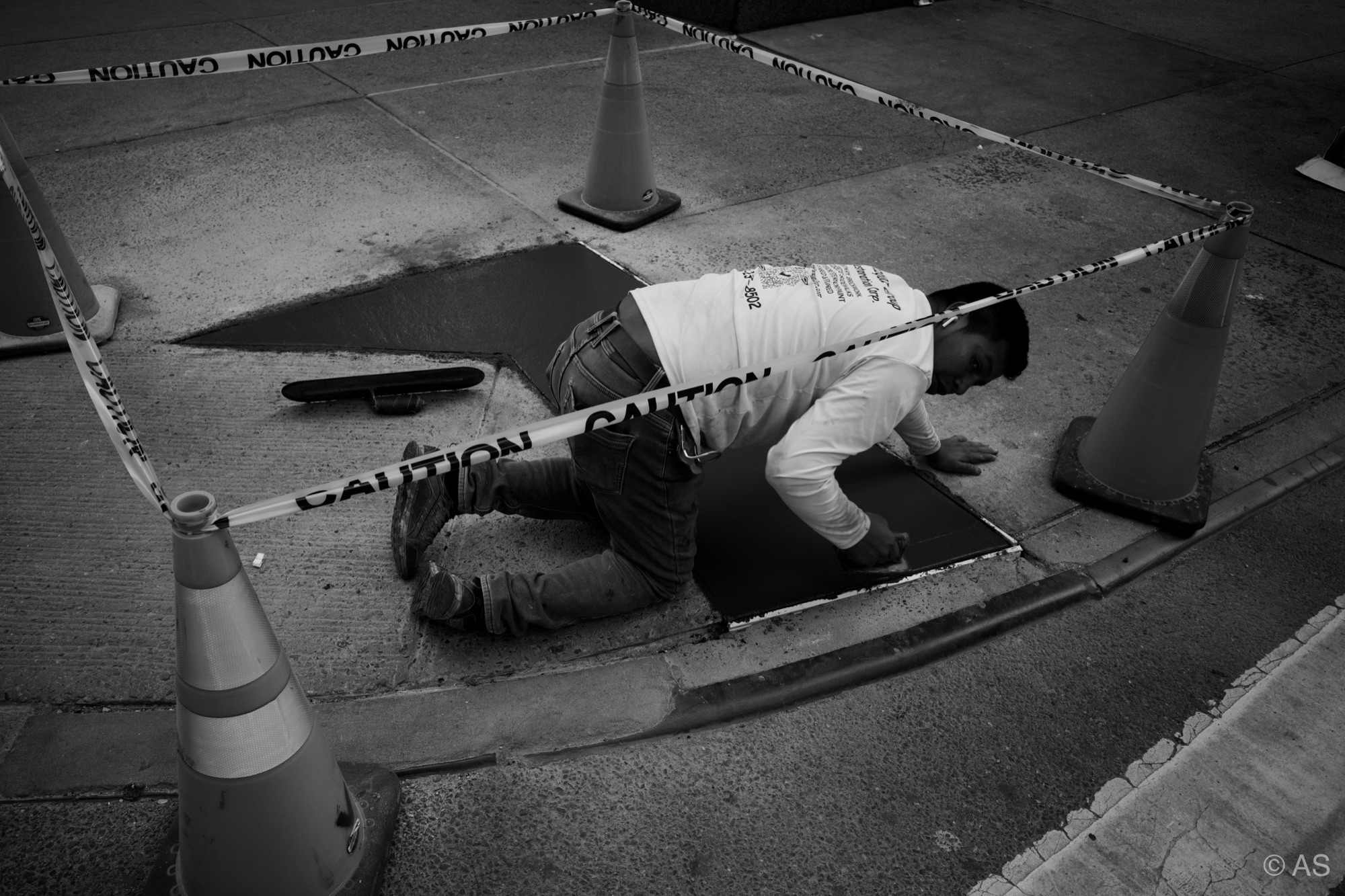 Man crawling under caution tape peering into an opening in the sidewalk