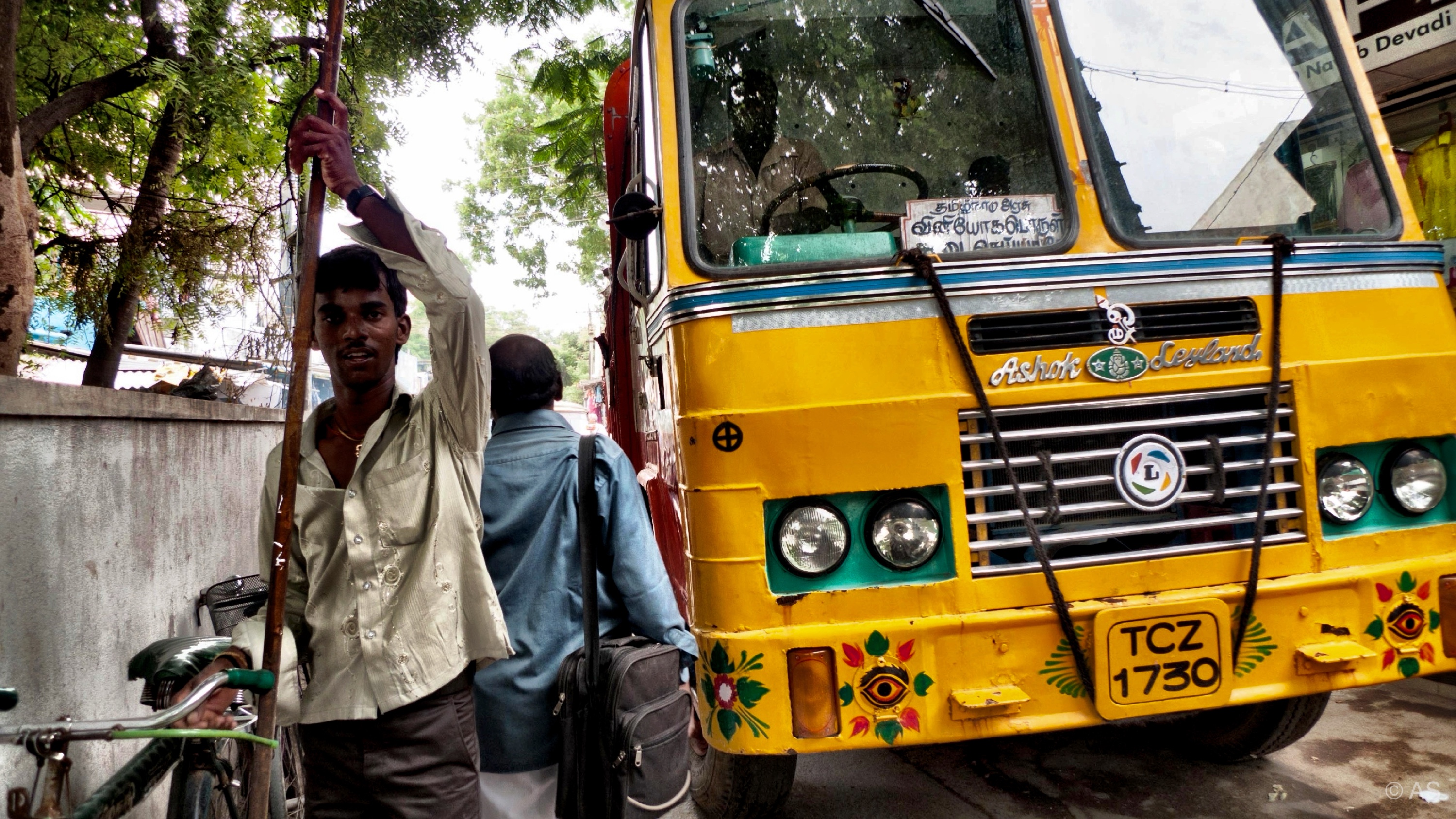 Man standing beside a bright yellow bus on a busy Indian street