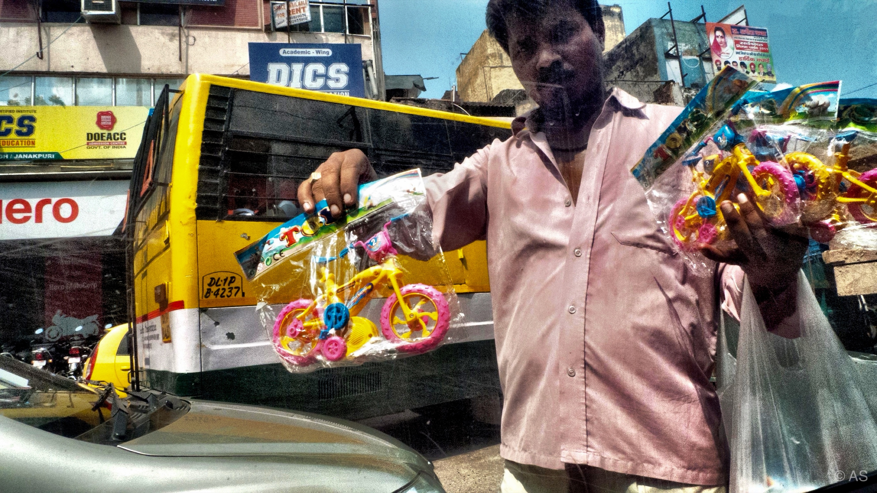 Street vendor selling colourful toy bicycles in front of a yellow bus