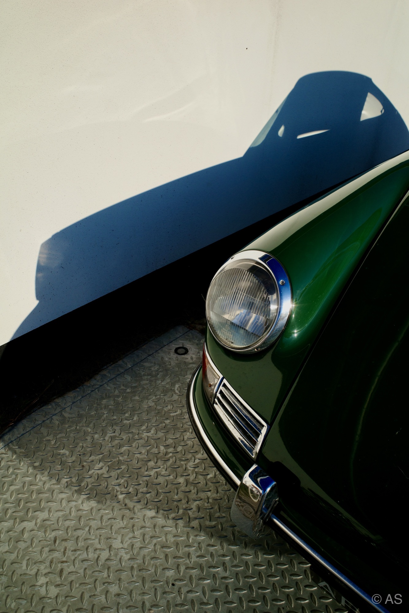 Detail of a vintage green car headlight casting a sharp shadow