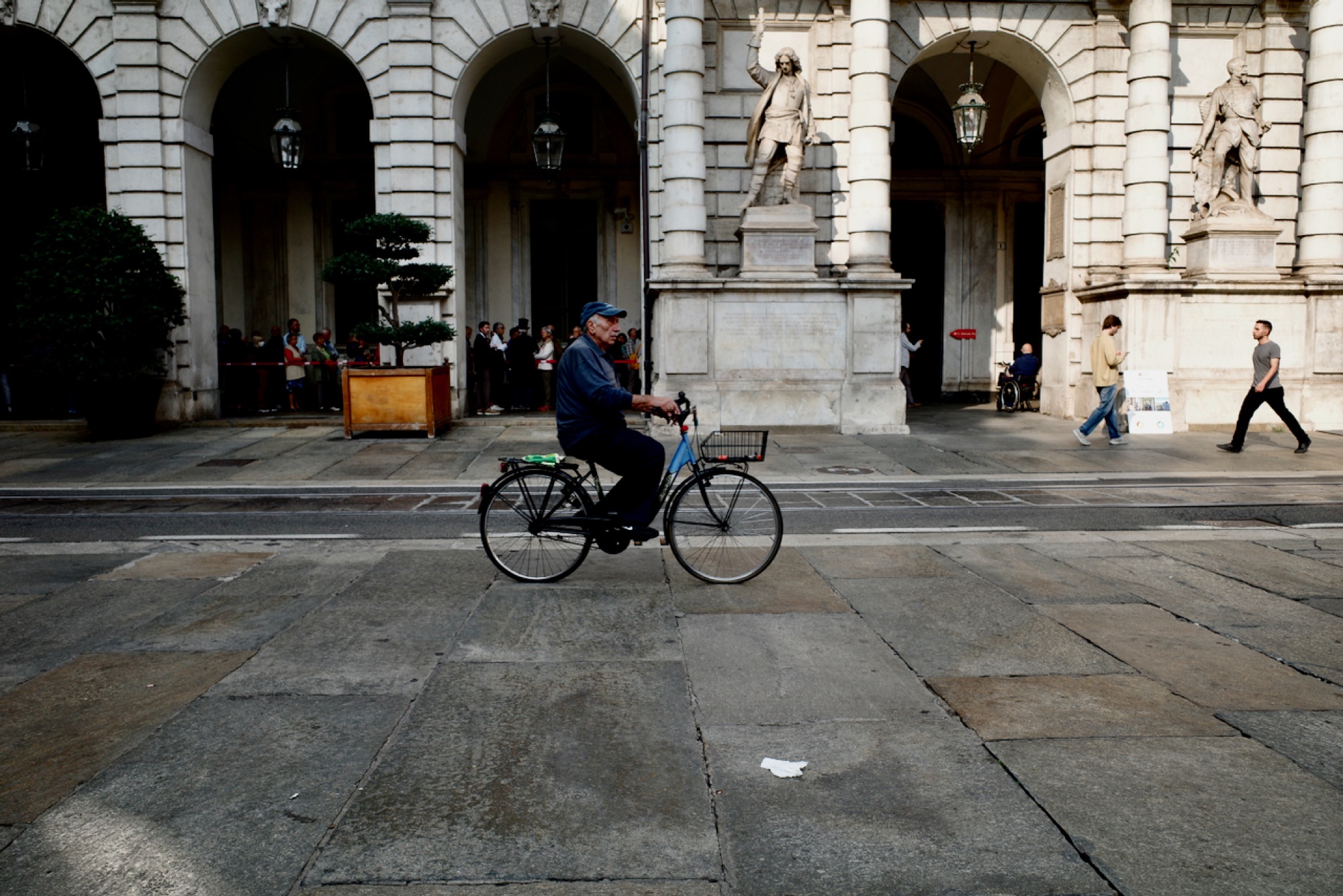 Cyclist riding past a grand European building with arched facades and classical statues
