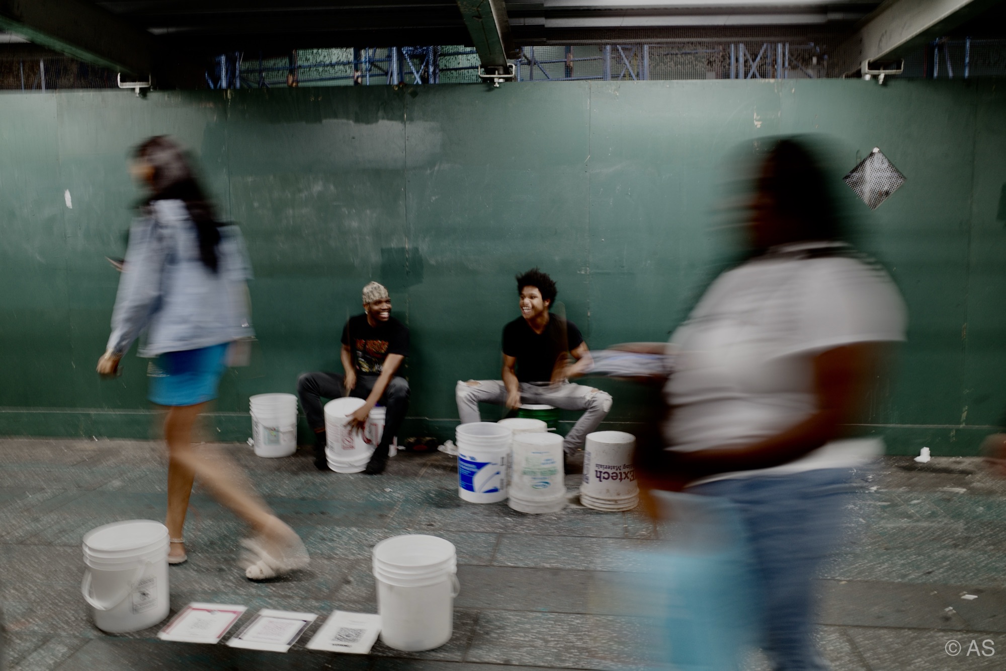 Street musicians playing bucket drums as pedestrians blur past