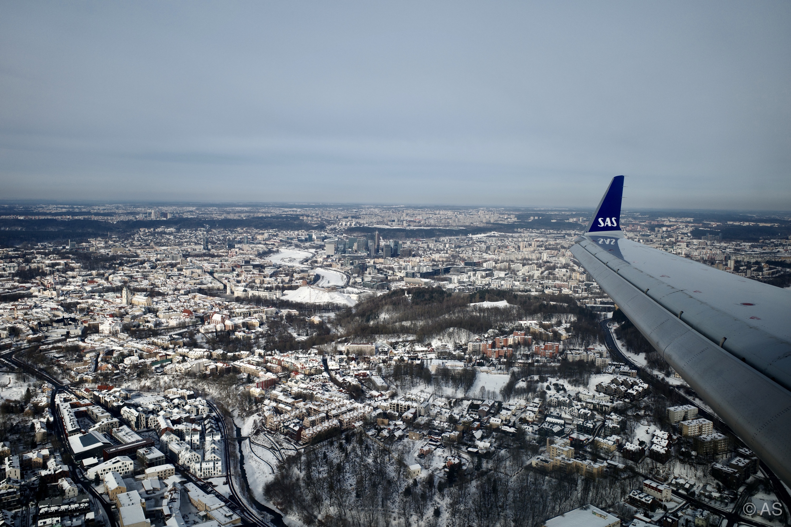 SAS plane wing over a snow-covered city seen from an aircraft window