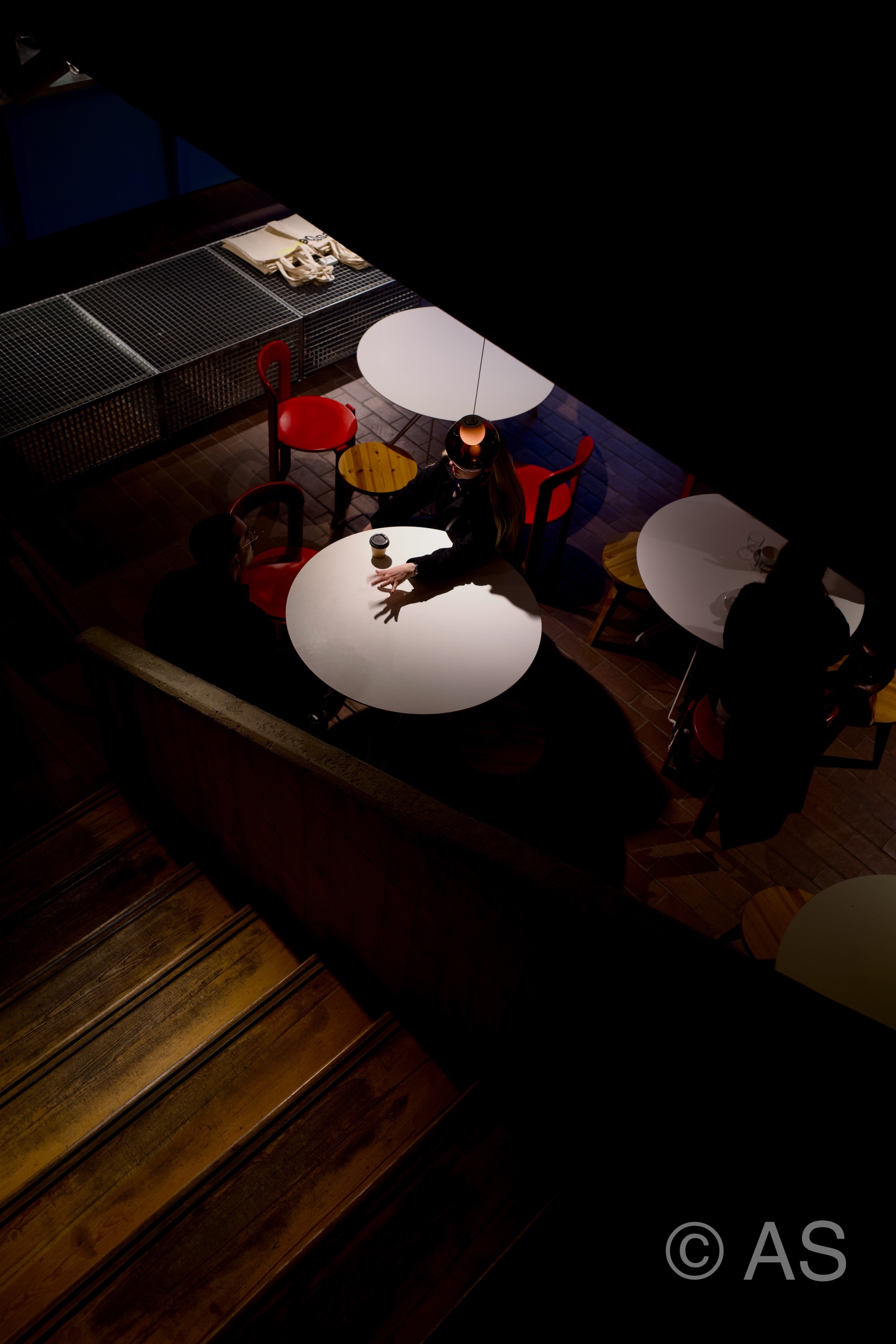 Overhead view of café tables lit by a spotlight with people gathered in darkness